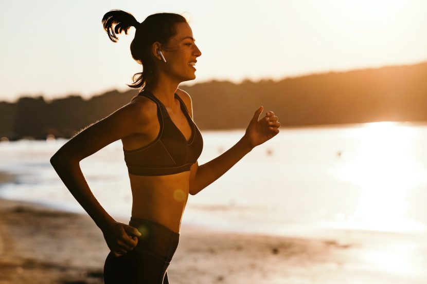 Motivated sportswoman running at riverside at sunset.