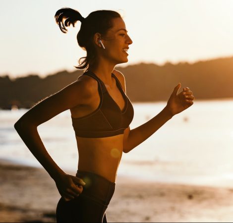 Motivated sportswoman running at riverside at sunset.